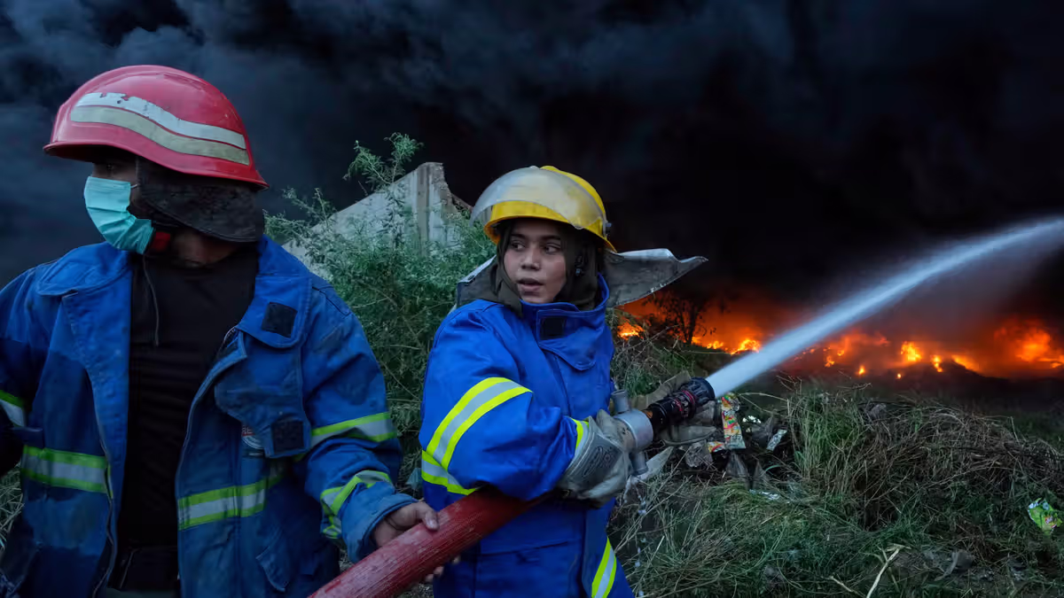 Female firefighter Syeda Masooma Zaidi, right, with her team member spray water to extinguish on a fire broke out in a storage facility packed vehicles tires, outskirts of Karachi, Pakistan, Thursday, Oct. 30, 2025. (AP Photo/Fareed Khan)